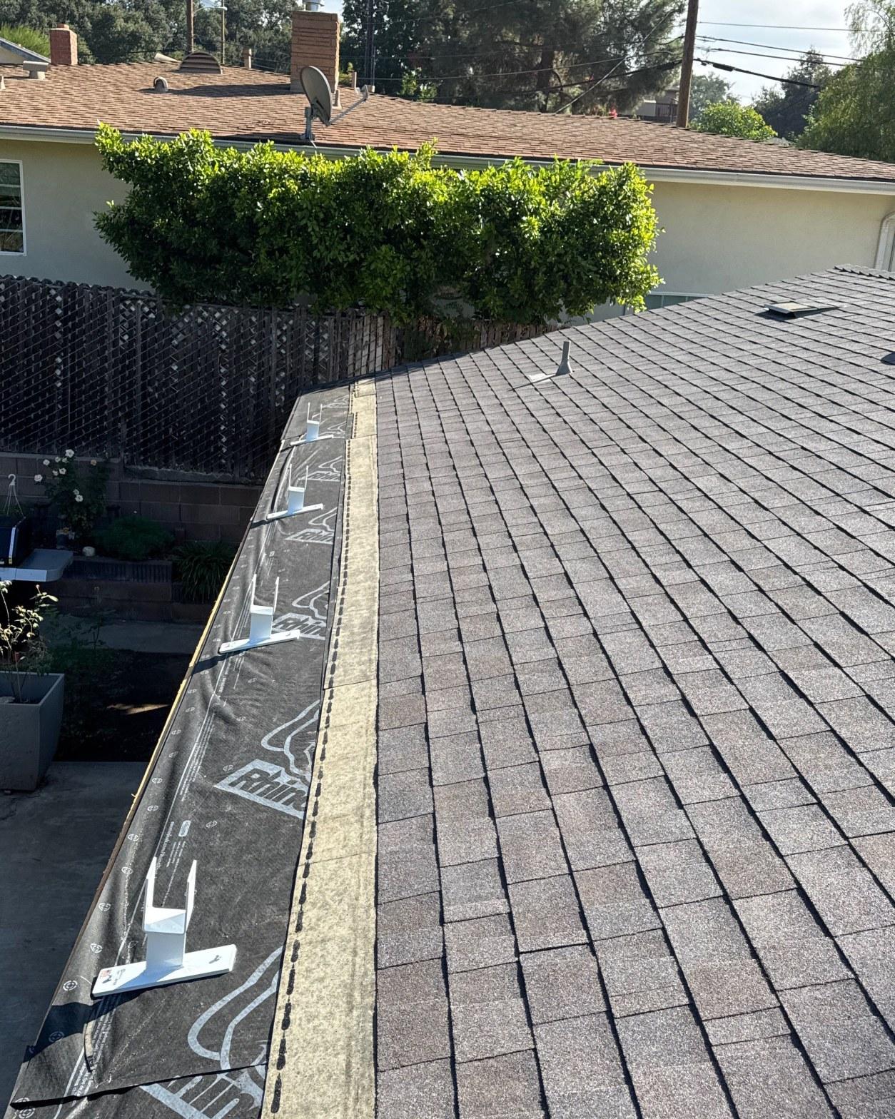 shingle-reroof-monrovia-3405 White solar panel roof mounts on gray asphalt shingles with roofing underlayment visible along eave edge.