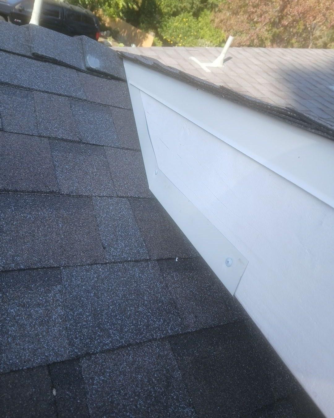 shingle-reroof-monrovia-3407 White aluminum seamless gutter fastened with screws at corner of dark asphalt shingle roof edge.