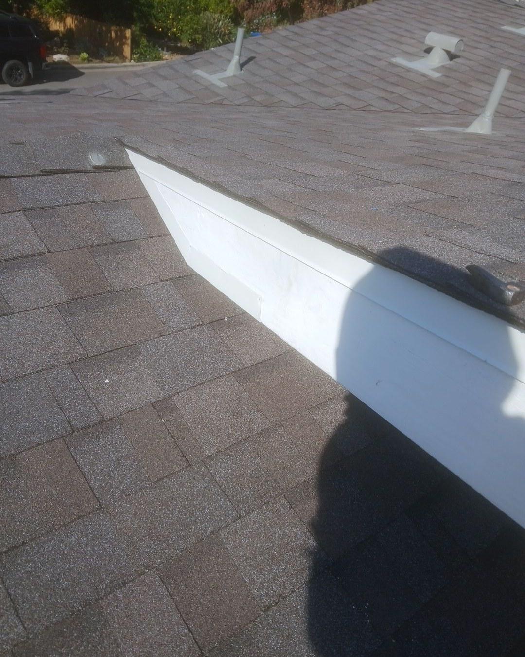 shingle-reroof-monrovia-3408 White rectangular skylight curb flashed into brown asphalt shingle roof with plumbing vents visible in background.