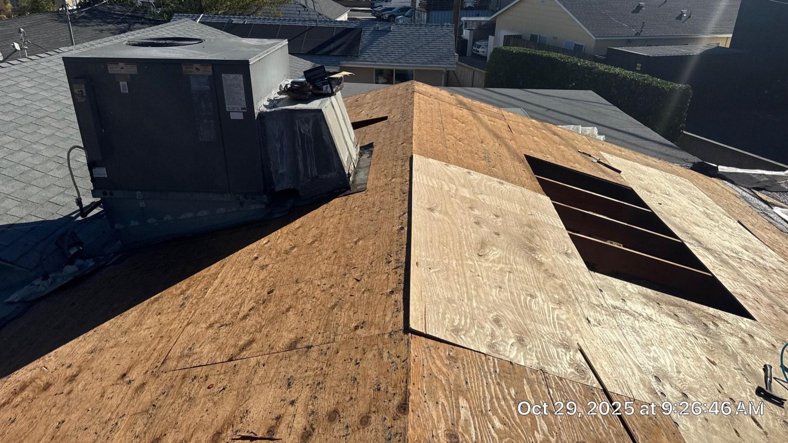 Exposed plywood roof decking with replacement panel near rooftop HVAC unit during shingle reroof on October 29 2025