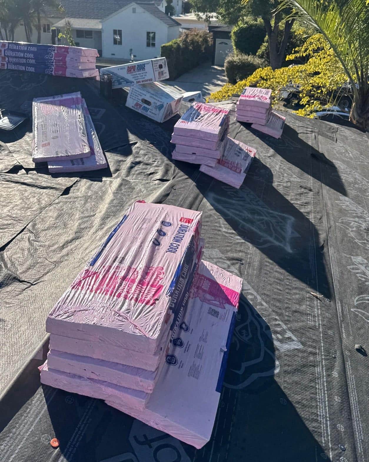 Owens Corning Duration Cool shingle bundles and Rapid Ridge cap staged across synthetic underlayment on a residential roof