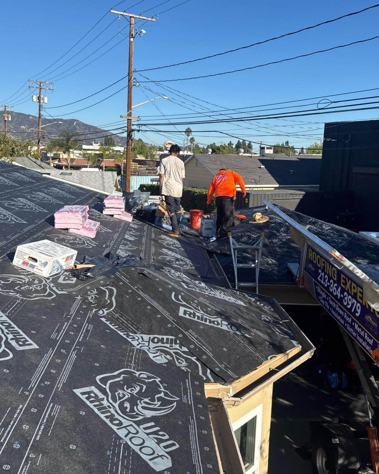 Roofing crew installing RhinoRoof U20 synthetic underlayment on multi-plane hip roof with Roof Replacement Inc truck visible
