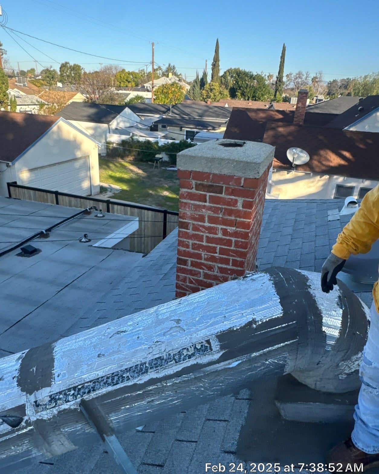 Fresh roofing cement applied to step flashing around brick chimney on completed composition shingle roof