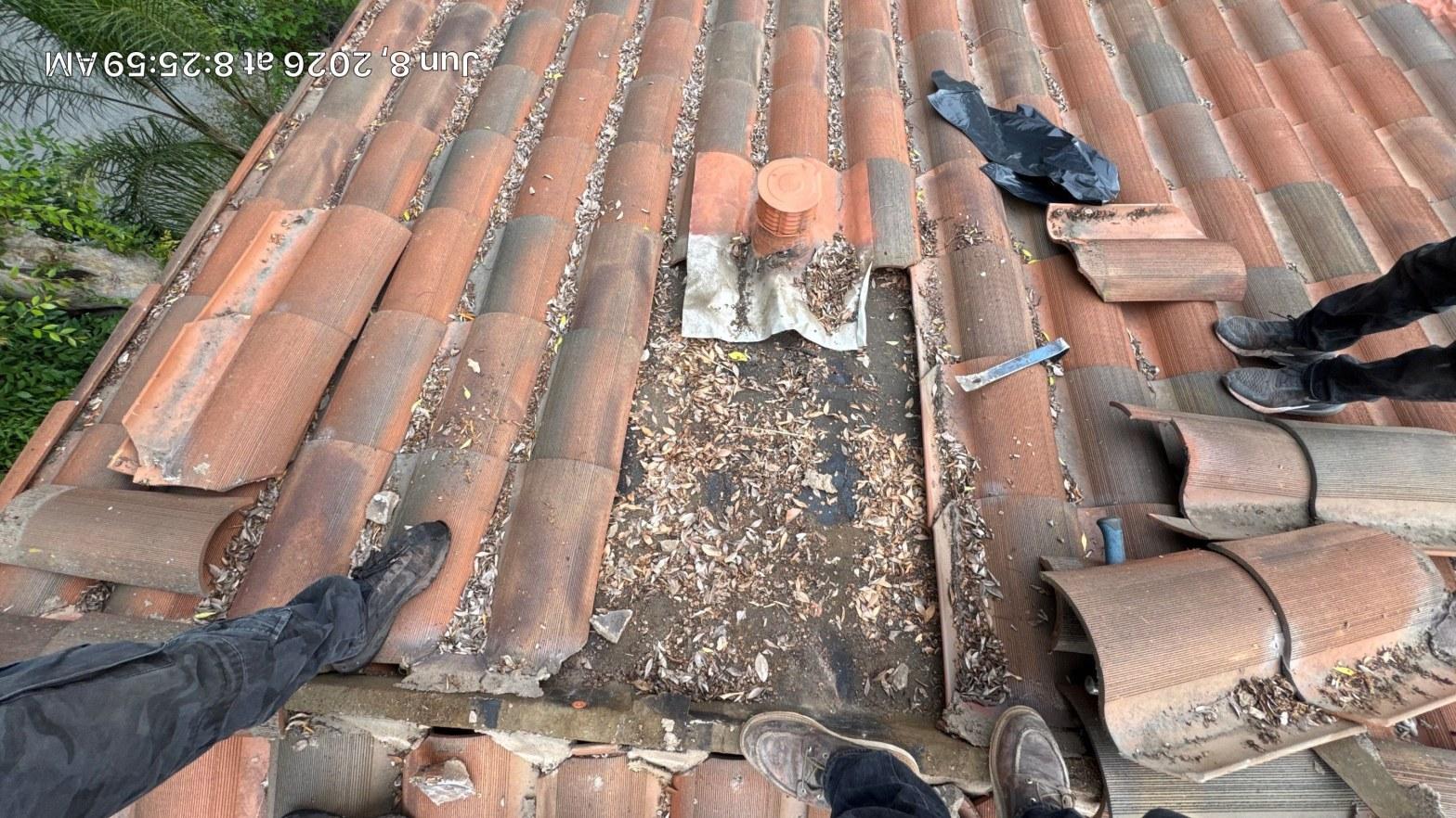 Roofers lifting clay tiles to expose deteriorated felt underlayment covered in years of debris on a Los Angeles County home