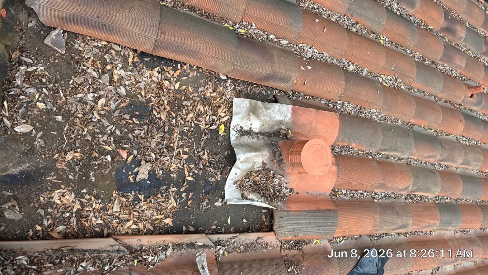 tile-roof-repair-vent-flashing-san-gabriel-3424 Clay tile roof with accumulated dead leaves, missing tiles exposing underlayment, and a pipe boot flashing visible.