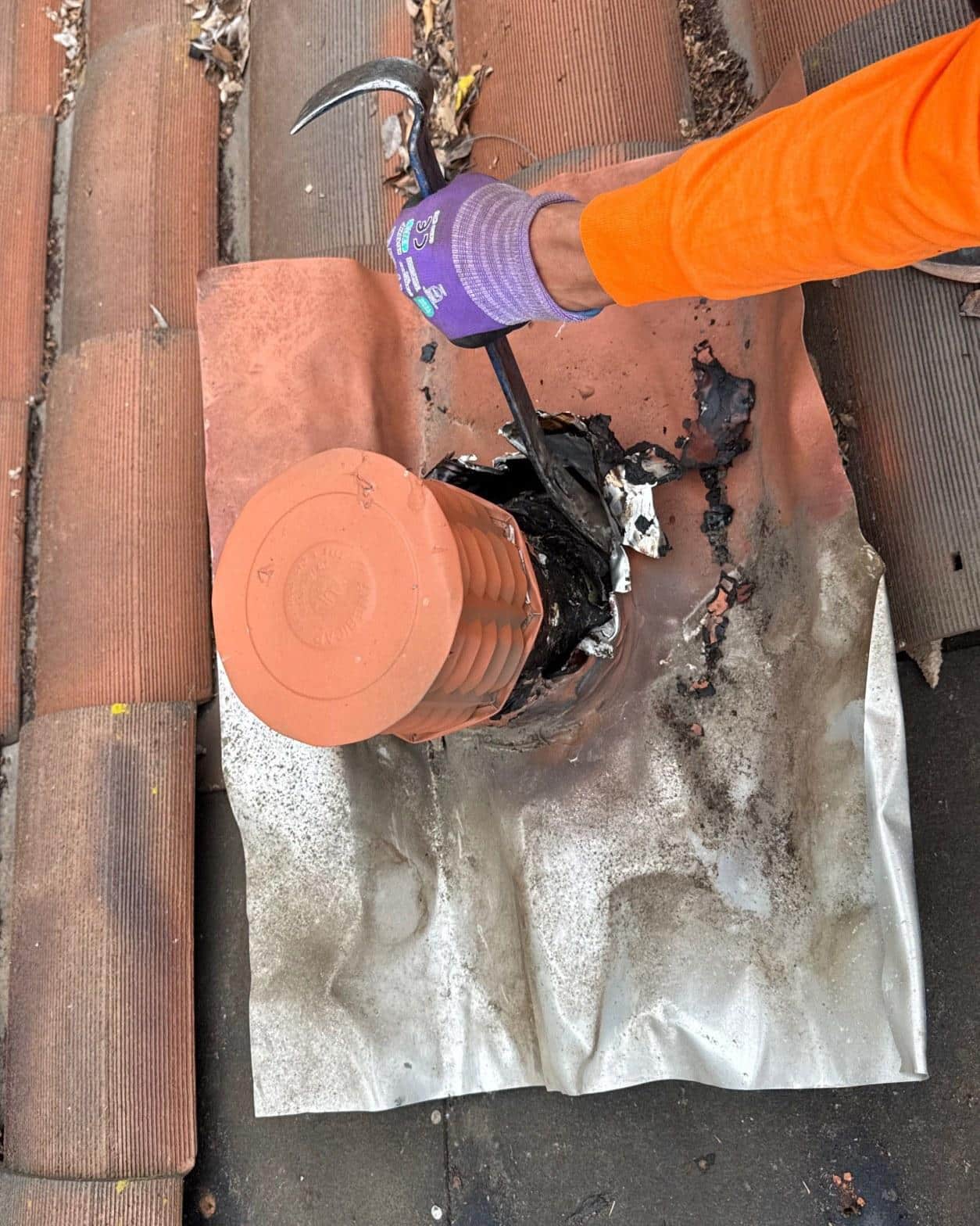 tile-roof-repair-vent-flashing-san-gabriel-3427 Gloved roofer using pry bar to remove deteriorated lead flashing around clay roof vent pipe on tile roof.