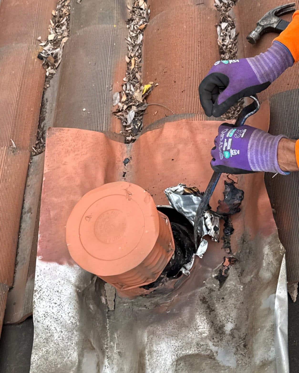 tile-roof-repair-vent-flashing-san-gabriel-3428 Gloved roofer using pry bar to remove deteriorated lead flashing around clay roof vent pipe on tiled roof.