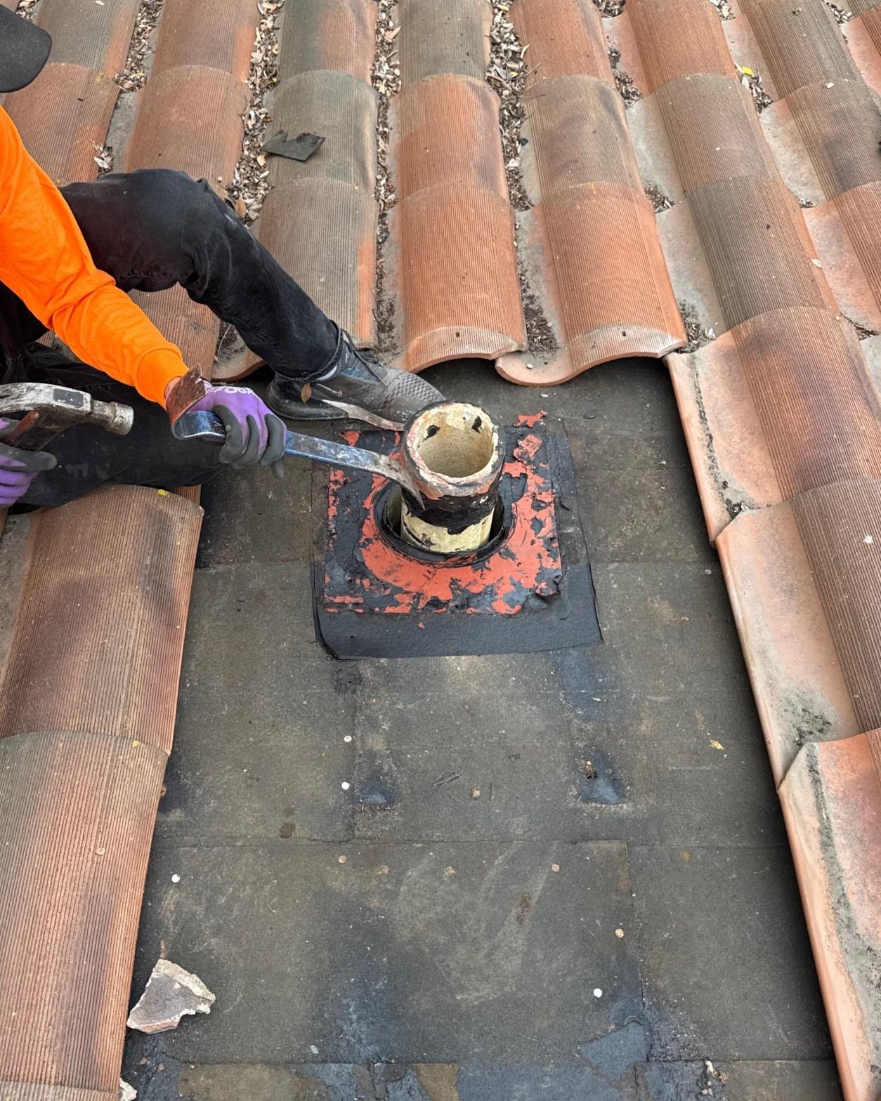 tile-roof-repair-vent-flashing-san-gabriel-3430 Roofer using pry bar to remove deteriorated rubber pipe boot flashing on clay tile roof during repair.