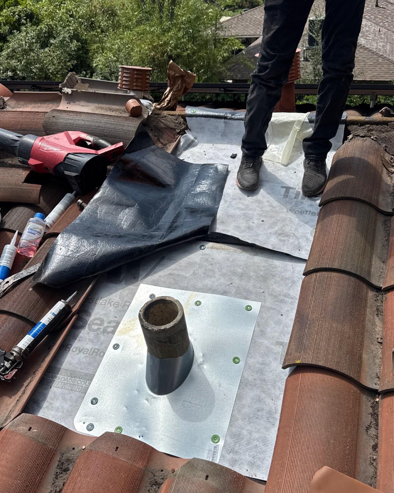 tile-roof-repair-vent-flashing-san-gabriel-3433 Roofer standing on tile roof installing pipe boot flashing with Milwaukee drill and sealant nearby.