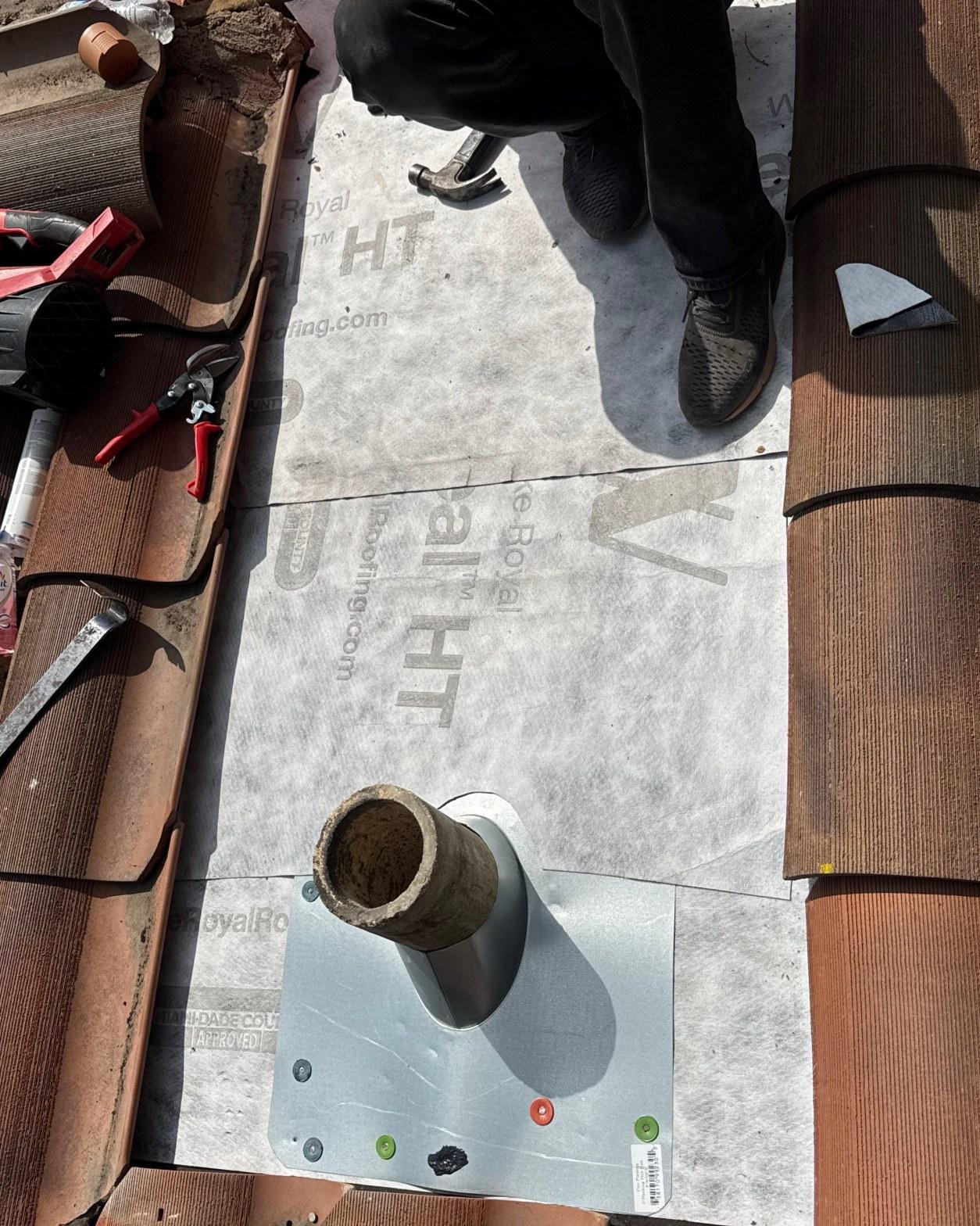 tile-roof-repair-vent-flashing-san-gabriel-3434 Pipe boot flashing and Royal HT underlayment being installed on clay tile roof by roofer holding hammer.