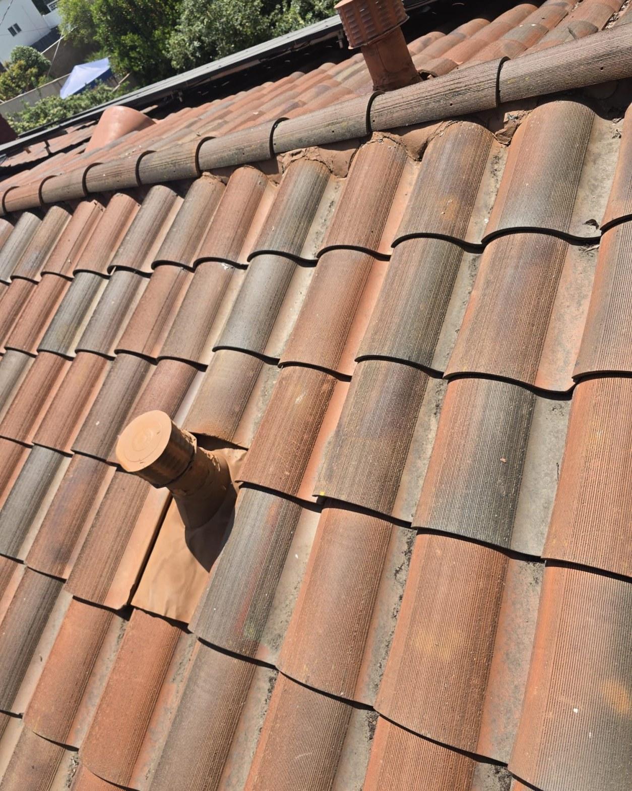 tile-roof-repair-vent-flashing-san-gabriel-3436 Aged terracotta clay barrel tile roof with copper pipe vent stack and ridge cap tiles, showing weathering.