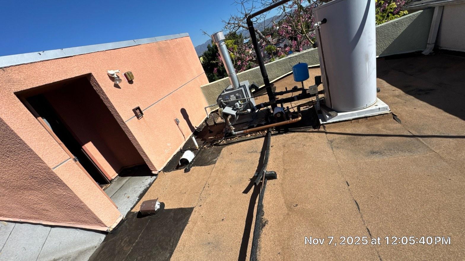 Deteriorated torch-down flat roof with exposed pipe penetrations and worn granulated cap sheet on apartment rooftop, San Fernando Valley