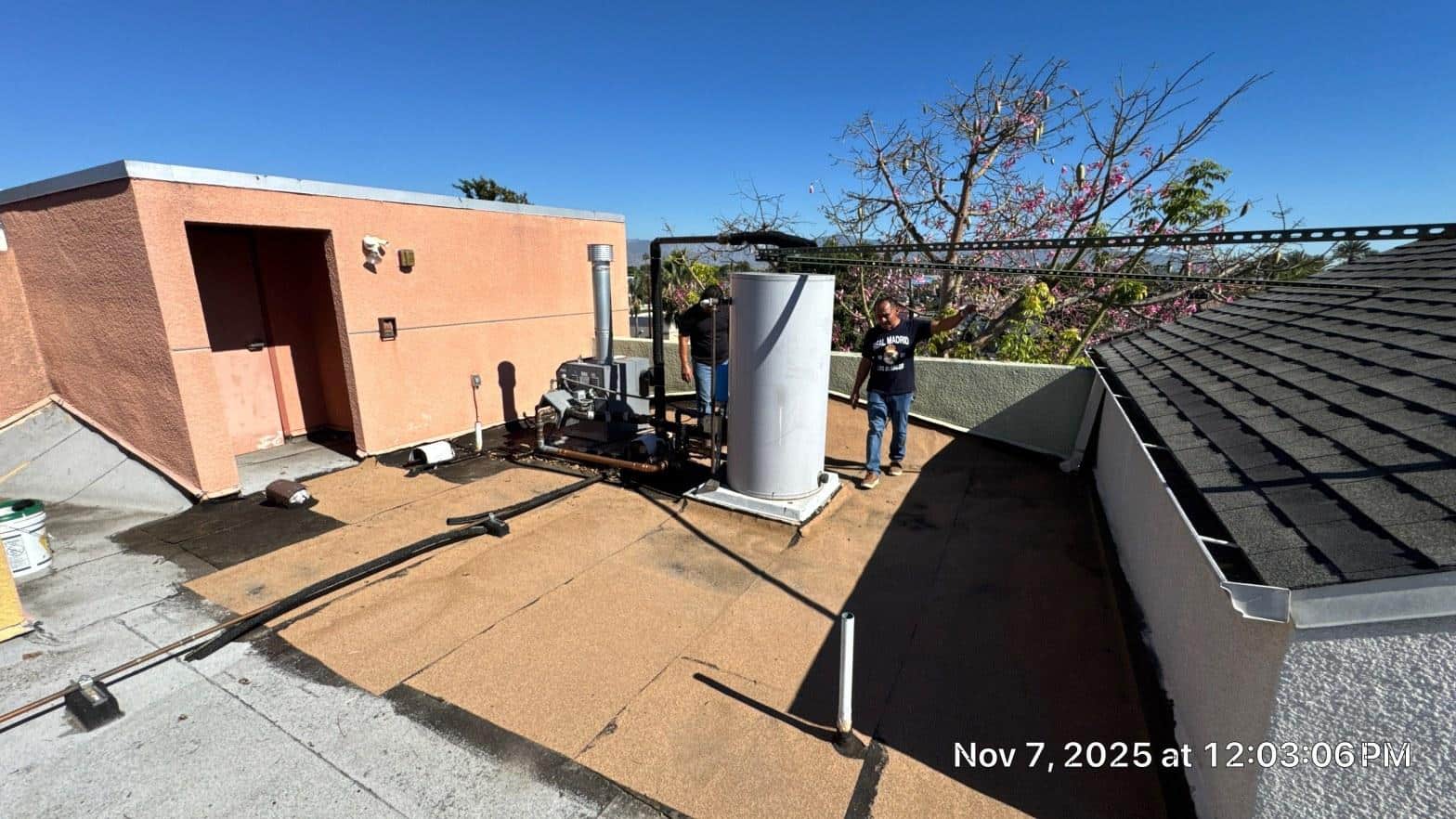 Roofing crew assessing rooftop boiler and copper pipe penetrations during flat roof replacement on multi-family apartment building