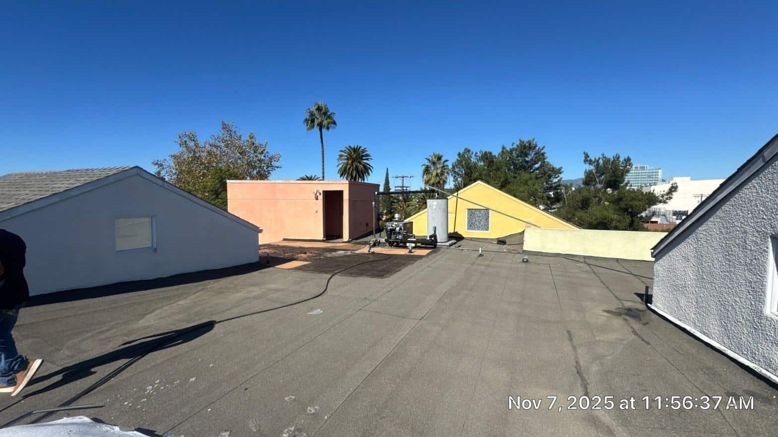 Newly installed torch-down modified bitumen cap sheet on low-slope apartment roof with parapet walls and palm trees in background