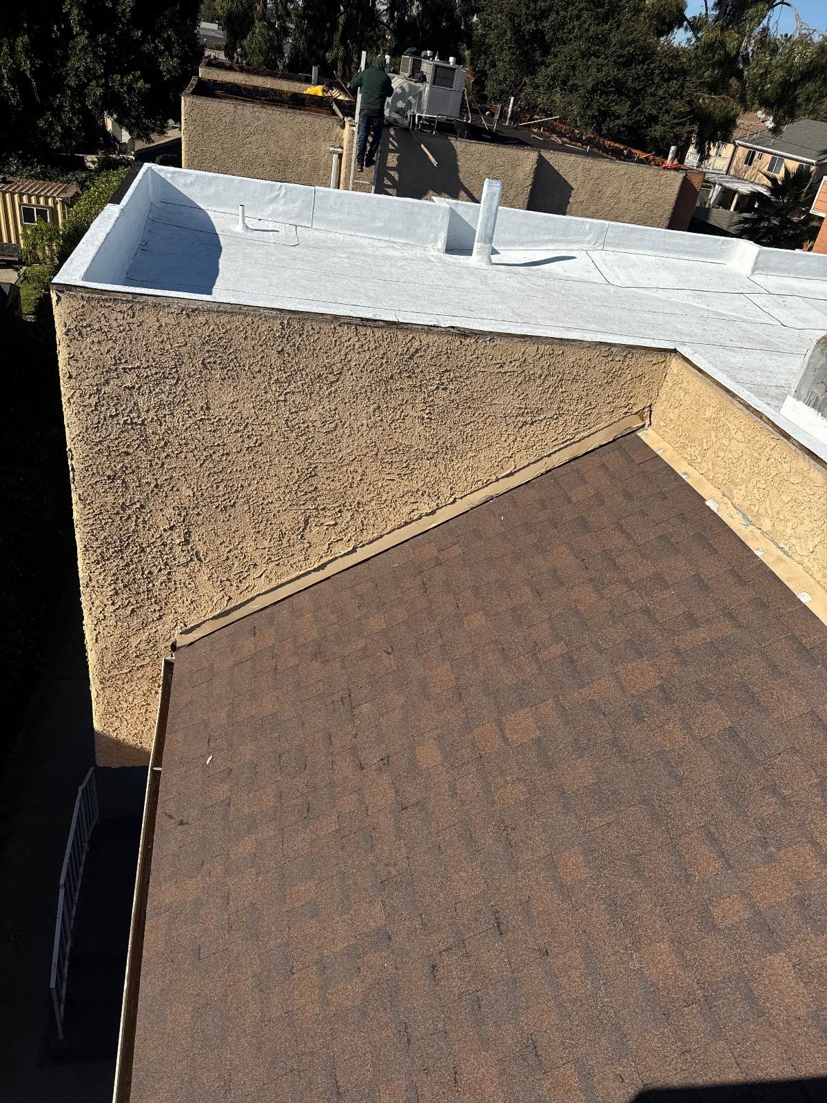 Flat TPO roof and brown asphalt shingle slope, stucco parapet wall, worker in background — Van Nuys — Roof Replacement Inc