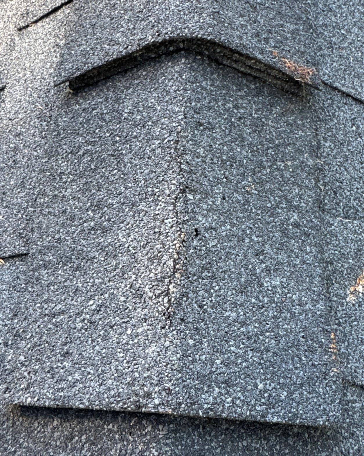 Close-up of a cracked asphalt shingle on a San Fernando Valley roof showing centerline thermal stress fracture and granule loss